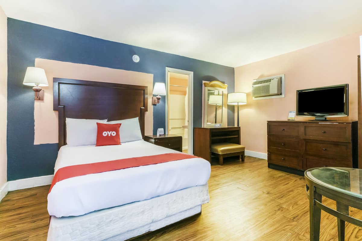 Habitación de hotel con una cama grande, piso de madera, escritorio, silla, televisor y cómoda.