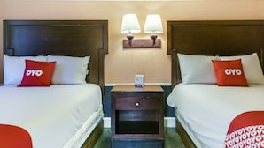 Habitación de hotel con dos camas, cada una con almohada roja de 'OYO', una mesita de noche con lámpara y una pequeña mesa con teléfono.