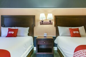 Une chambre d’hôtel avec deux lits, chacun agrémenté d’un oreiller rouge orné du logo « OYO », une table de chevet avec une lampe et une petite table avec un téléphone.