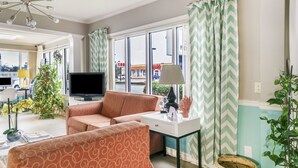 Una sala de estar con un sofá, televisor, lámpara y una ventana con cortinas.