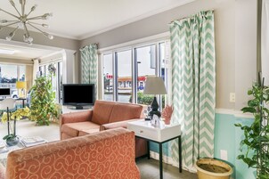 Un salon avec un canapé, un téléviseur, une lampe et une fenêtre avec des rideaux.