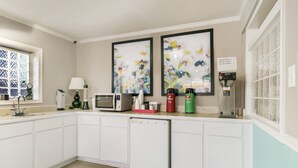 Una cocina moderna con armarios blancos, un microondas, una cafetera y dos cuadros florales en la pared.