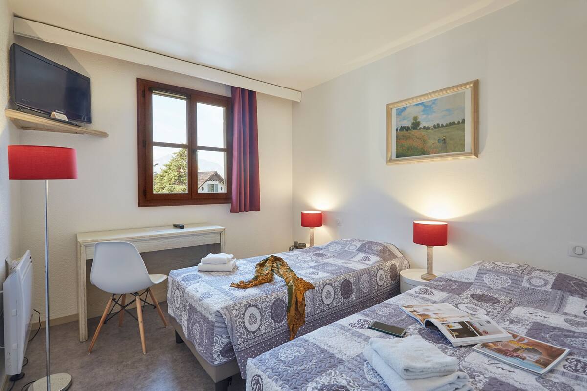 Un dormitorio con dos camas, un escritorio, una silla, un televisor y un cuadro en la pared.