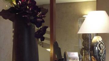 A room with a large mirror, a vase with flowers, a lamp, and a small table with a book and a decorative item.
