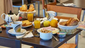 Una mesa de desayuno con croissants, zumo de naranja y cereales.