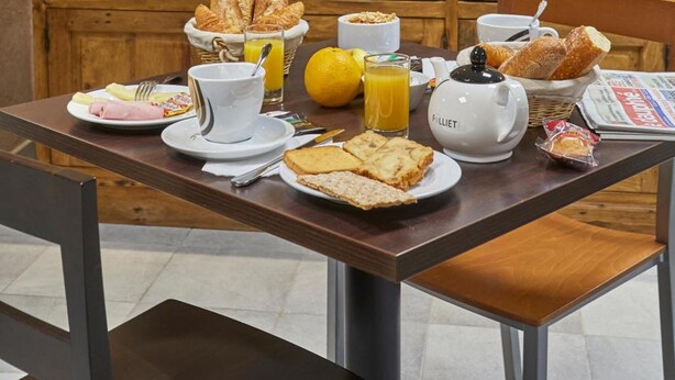 A breakfast setup with a variety of food items, including bread, pastries, and beverages, arranged on a wooden table with a wicker basket. - Cit’Hôtel Le National (Cluses)
