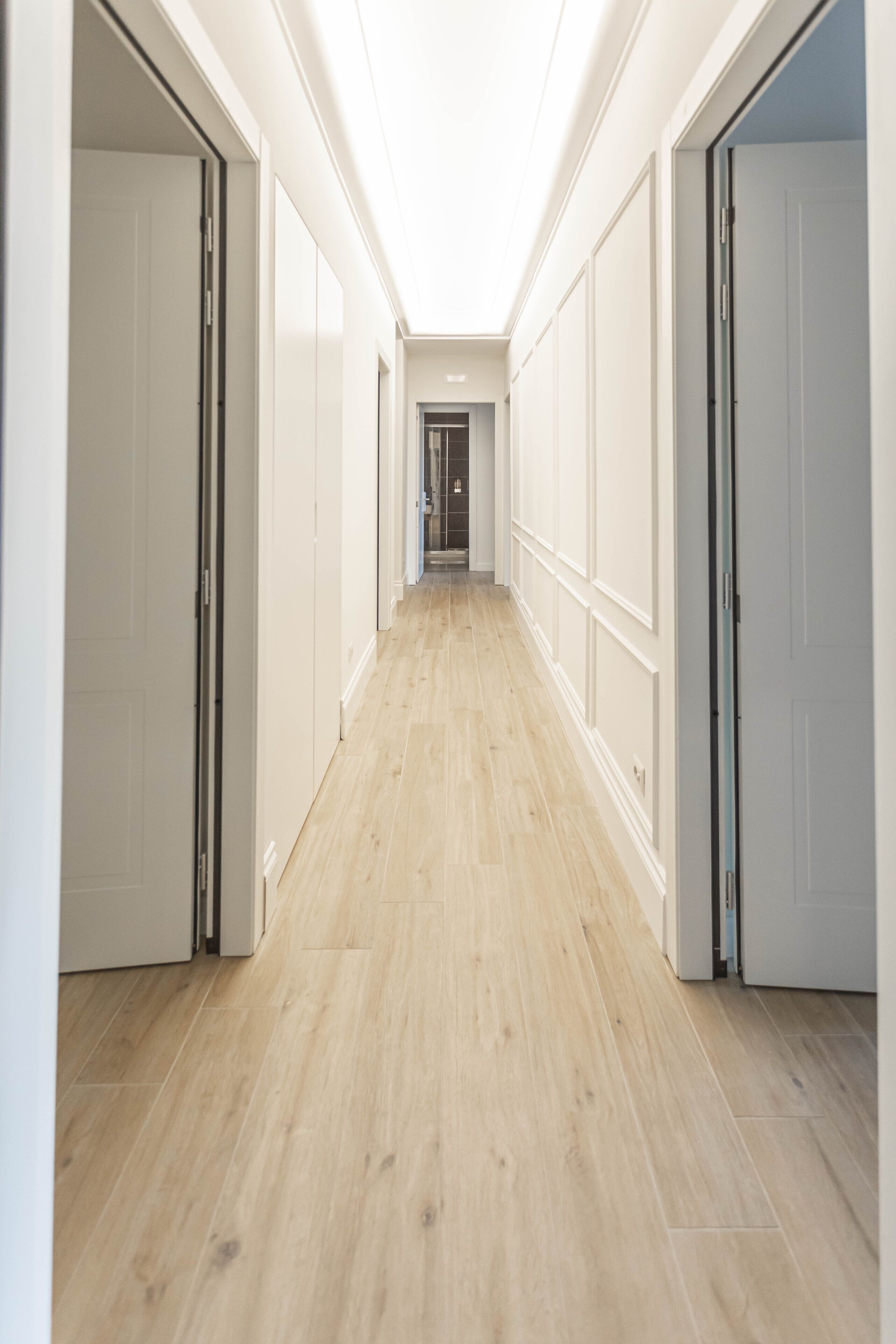 A hallway with wooden flooring and white walls, leading to a door at the end.