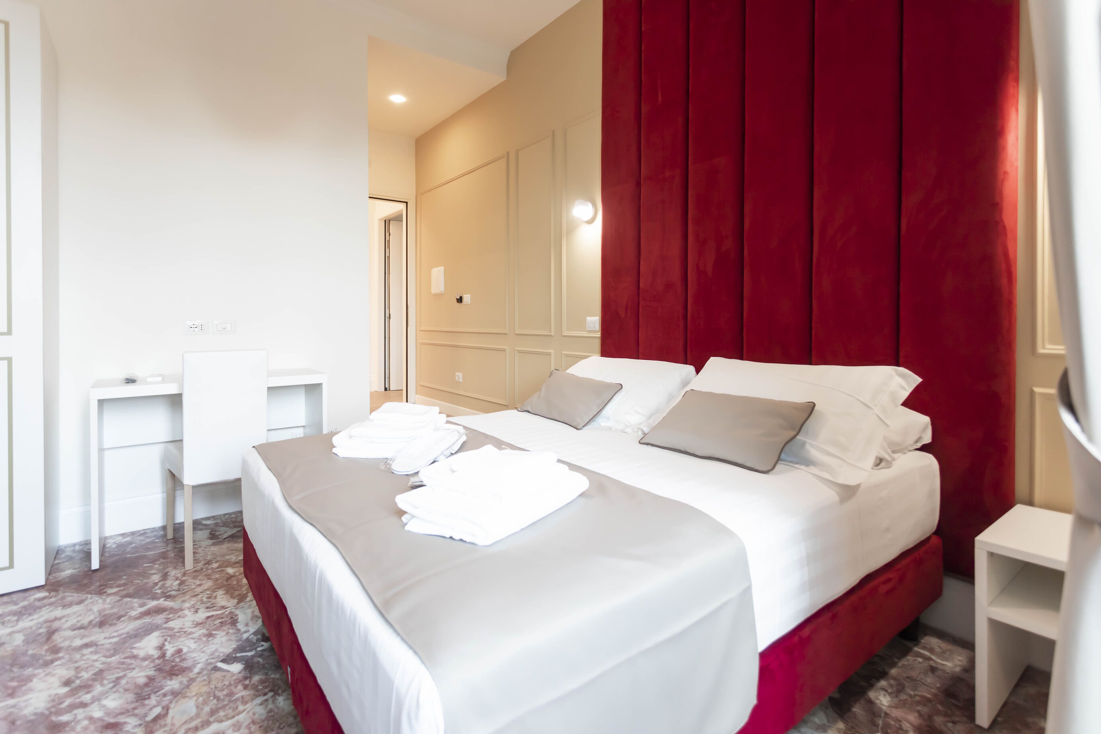 A hotel room with a neatly made bed, a desk, and a red accent wall.