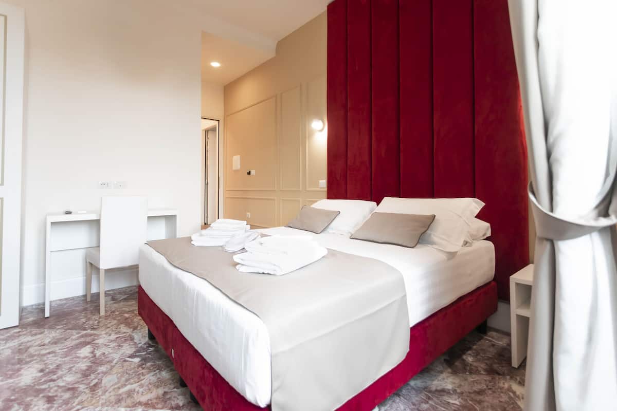 A hotel room with a large bed, a desk, and a red accent wall.