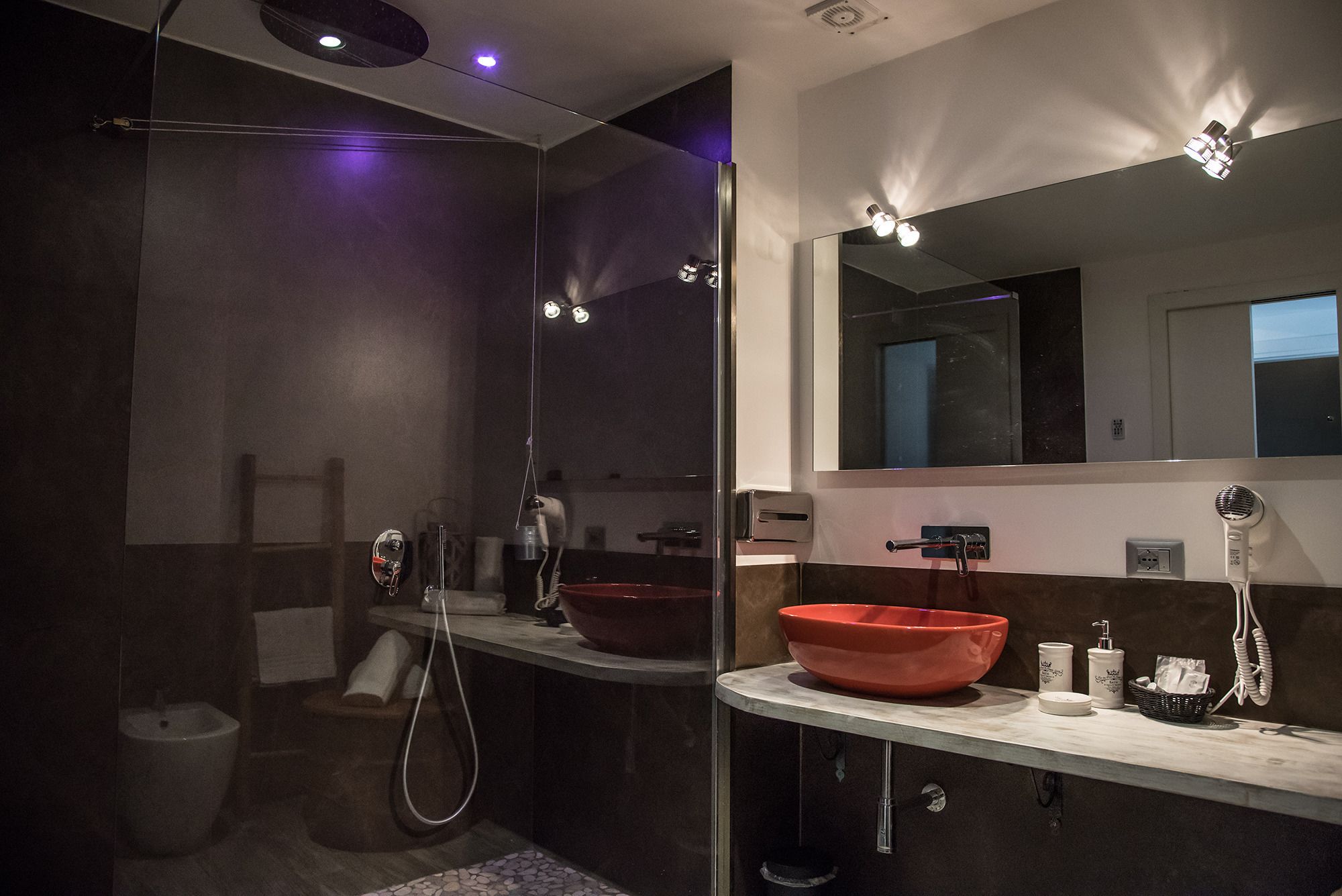 A modern bathroom with a glass-enclosed shower, a large mirror, and a red basin.