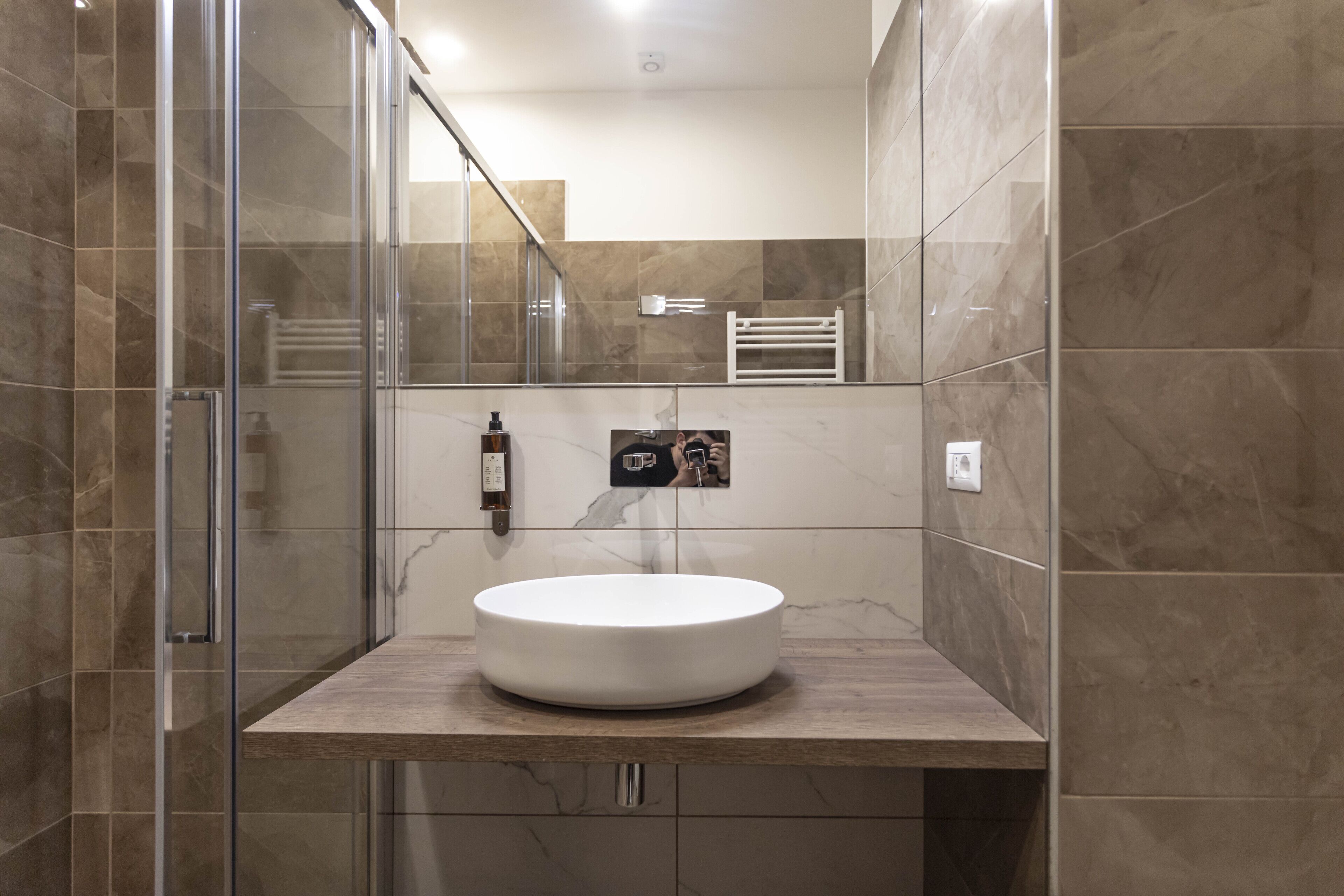 Un baño moderno con ducha de vidrio, lavamanos blanco y azulejos de mármol.