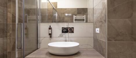 Un baño moderno con ducha de vidrio, lavamanos blanco y azulejos de mármol.