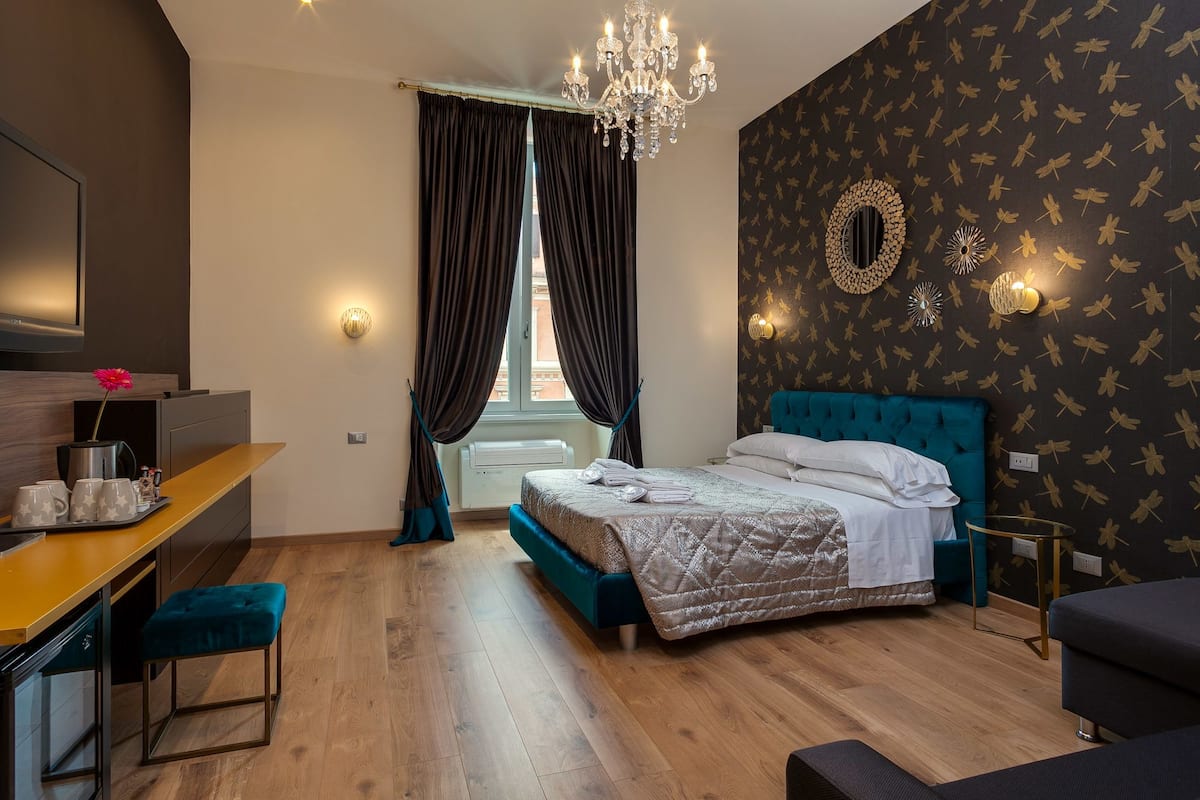A bedroom with a bed, a desk, a chair, a chandelier, and a window with curtains.