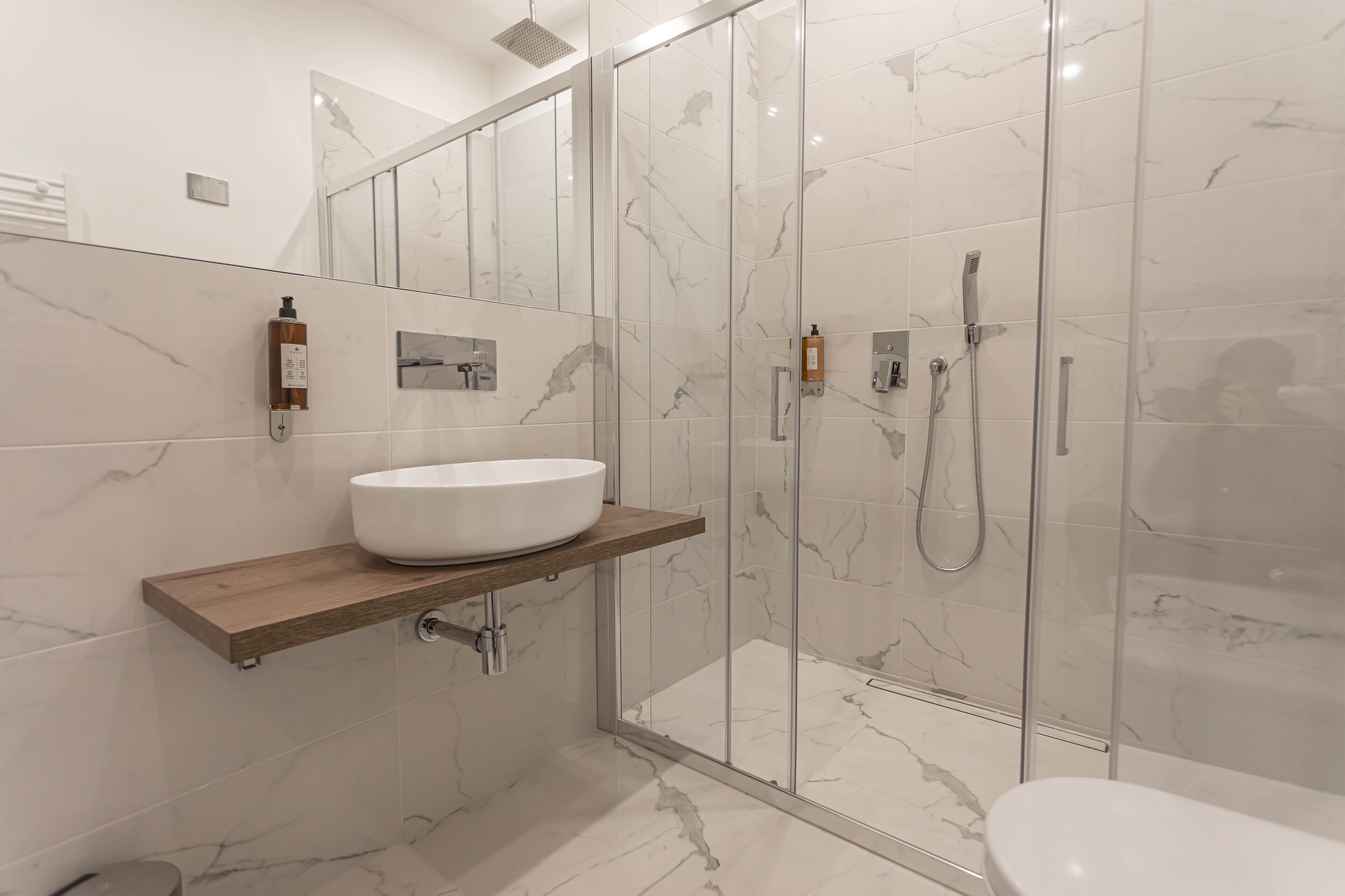 Un baño moderno con un lavamanos grande de color blanco, una ducha con cerramiento de vidrio y paredes cubiertas de mármol.