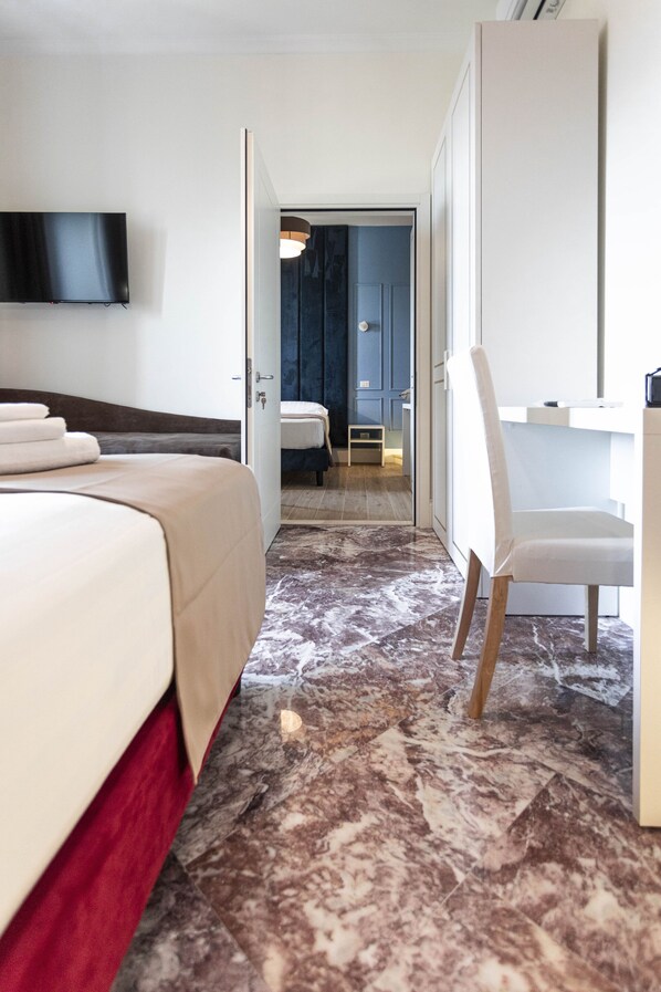 A hotel room with a bed, a desk, a chair, a TV mounted on the wall, and a bathroom visible through an open door.