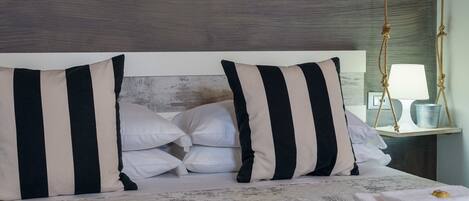 Una cama bien hecha con almohadas a rayas, una lámpara de noche y toallas dobladas ordenadamente sobre una colcha estampada.
