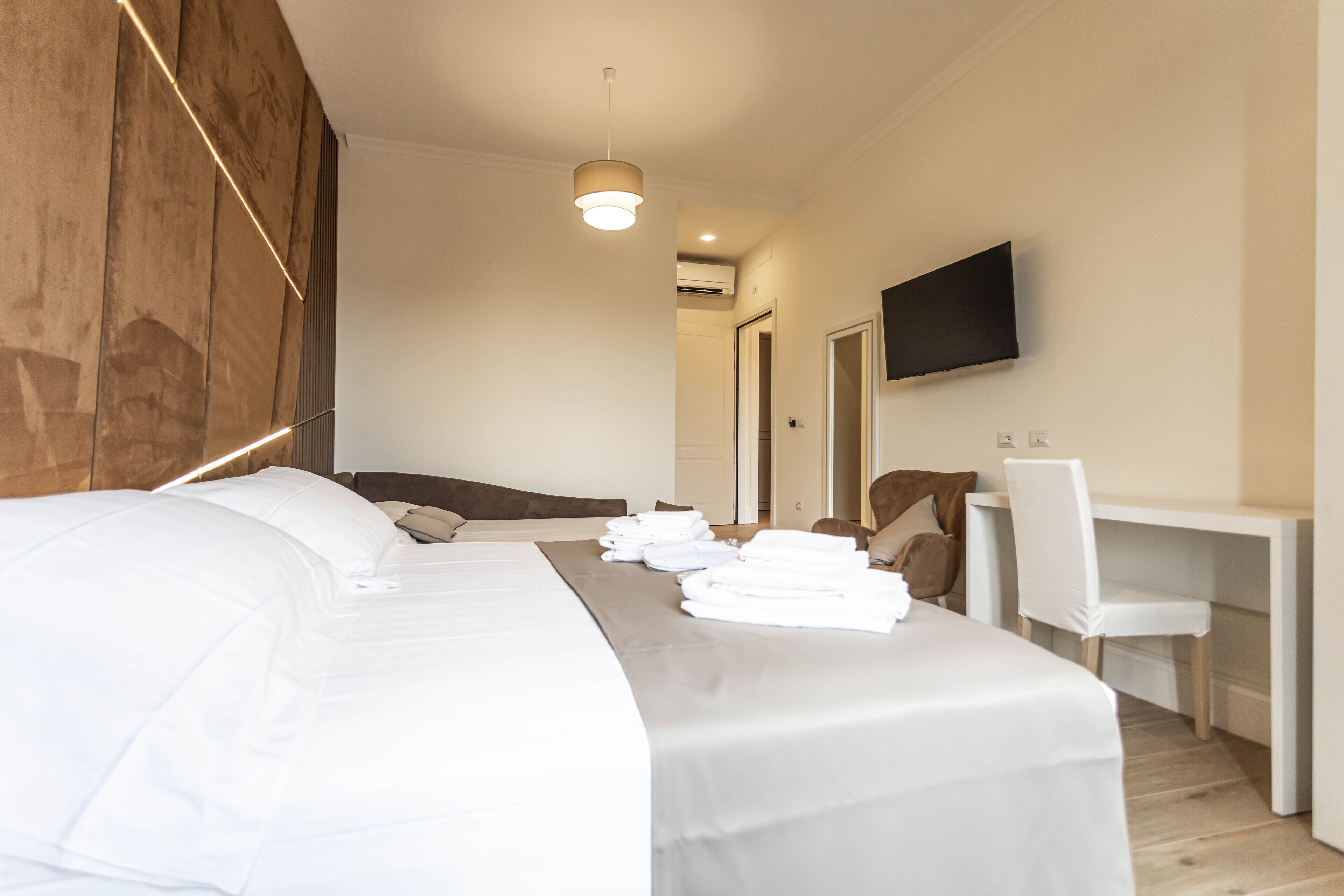 A hotel room with a large bed, a desk, a chair, and a flat-screen TV mounted on the wall.