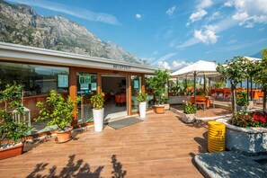A reception area with a mountain backdrop, outdoor seating, and potted plants. - Garda Suite Hotel  (Limone sul Garda)