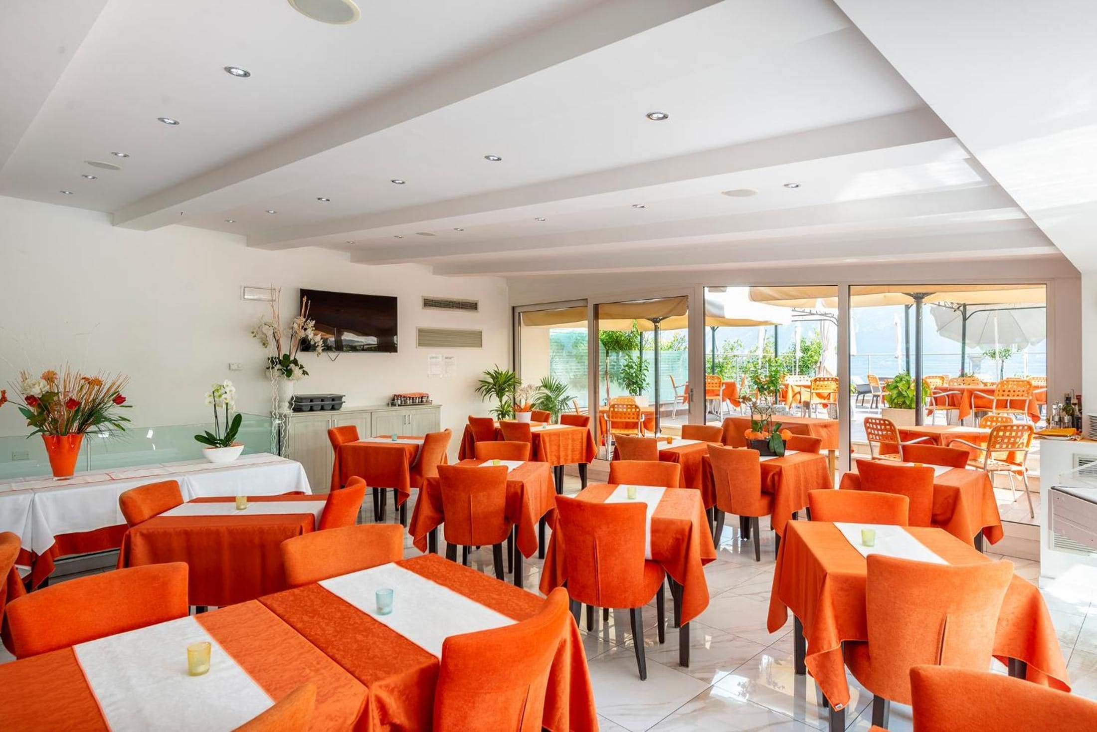 Ein Restaurant mit mehreren Tischen und Stühlen, einem Flachbildfernseher an der Wand und Blick ins Freie.