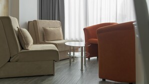 A modern living room with a beige sofa, an orange armchair, and a small glass table. - Garda Suite Hotel  (Limone sul Garda)