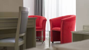 A modern hotel room with a wooden chair, a glass table, and two red armchairs.