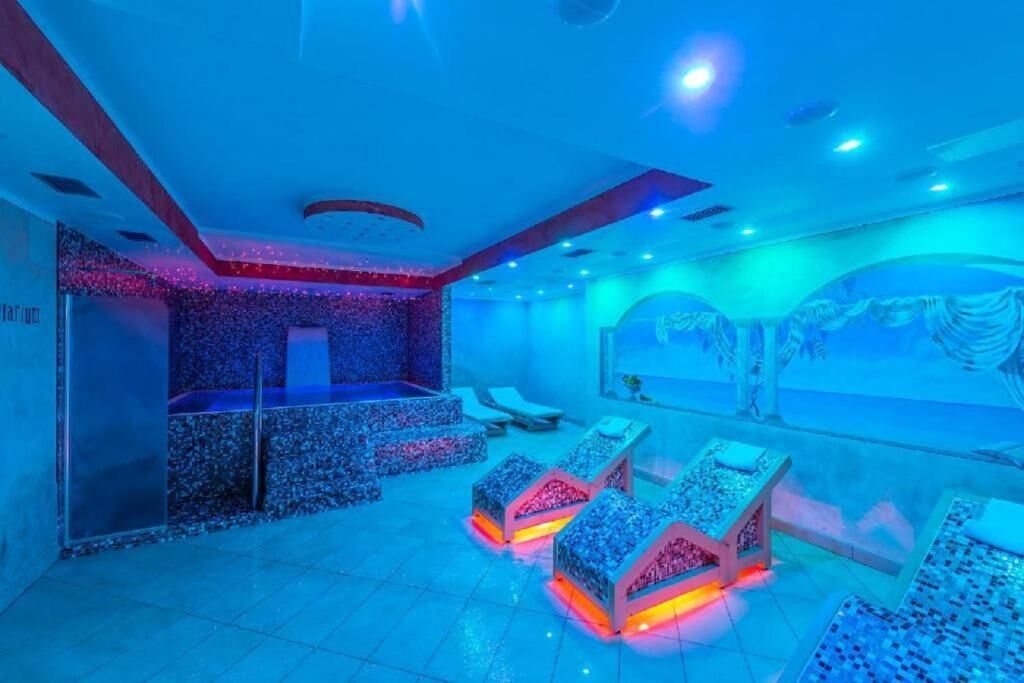 Une pièce comprenant un espace de massage éclairé de lumière bleue, un comptoir d’accueil et un coin salon avec des tables de massage.