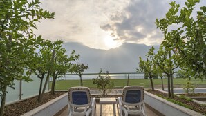 An outdoor seating area with two chairs and a table, surrounded by trees and a view of a body of water and mountains. - Garda Suite Hotel  (Limone sul Garda)