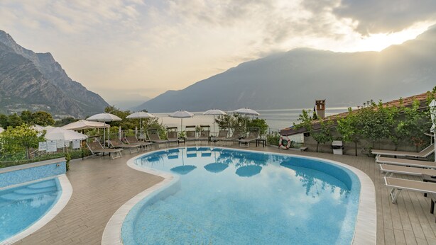 A swimming pool with lounge chairs and umbrellas, surrounded by mountains and a view of the sea. - Garda Suite Hotel  (Limone sul Garda)