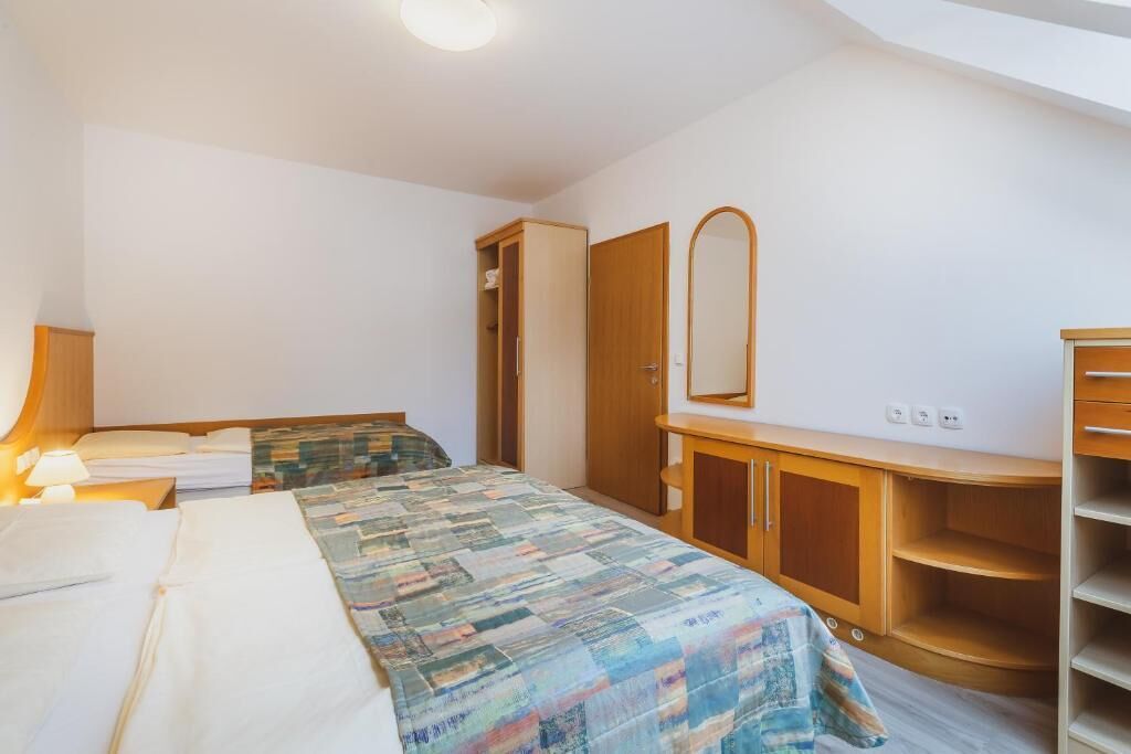 A bedroom with a bed, a wardrobe, a mirror, and a bedside table with a lamp.