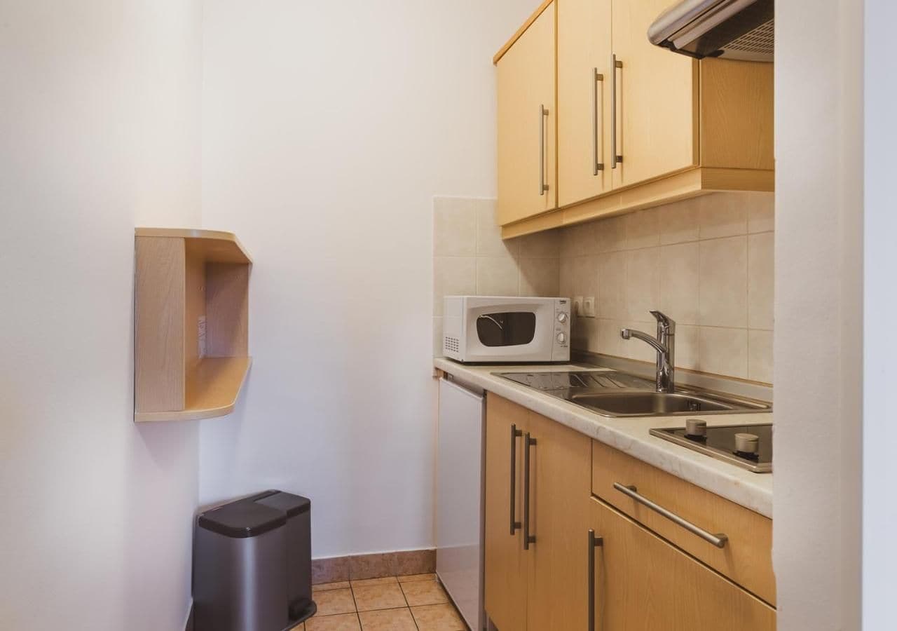 A compact kitchen with a microwave, sink, and wooden cabinets.