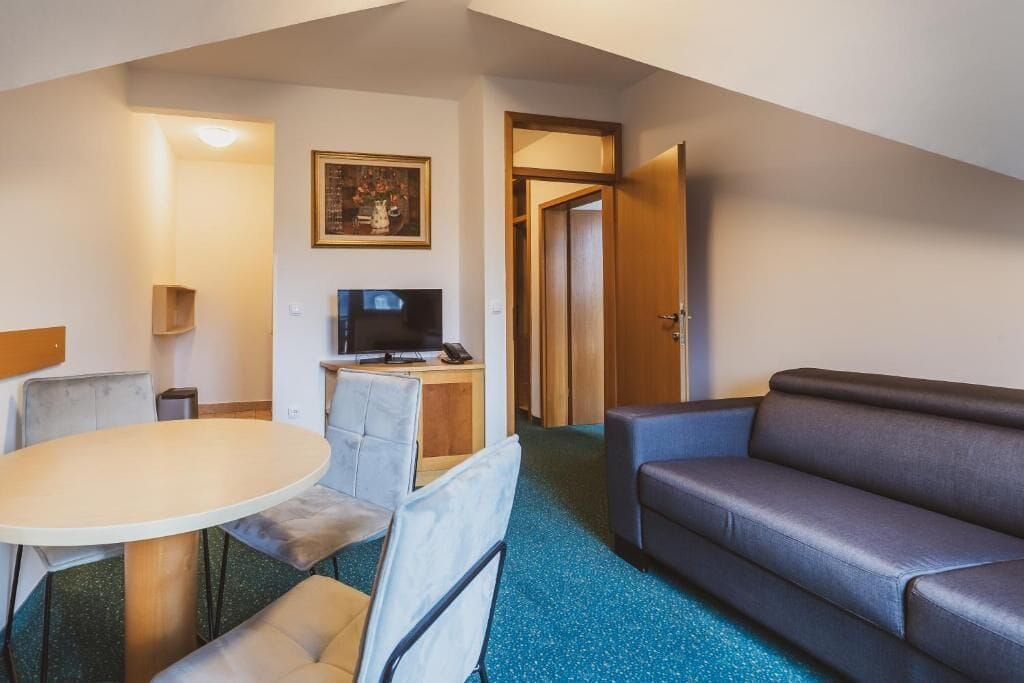 Ein Hotelzimmer mit Esstisch, Stühlen, einer Sitzecke, einem Fernseher und einem gerahmten Bild an der Wand.