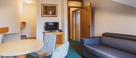 Ein Hotelzimmer mit Esstisch, Stühlen, einer Sitzecke, einem Fernseher und einem gerahmten Bild an der Wand.