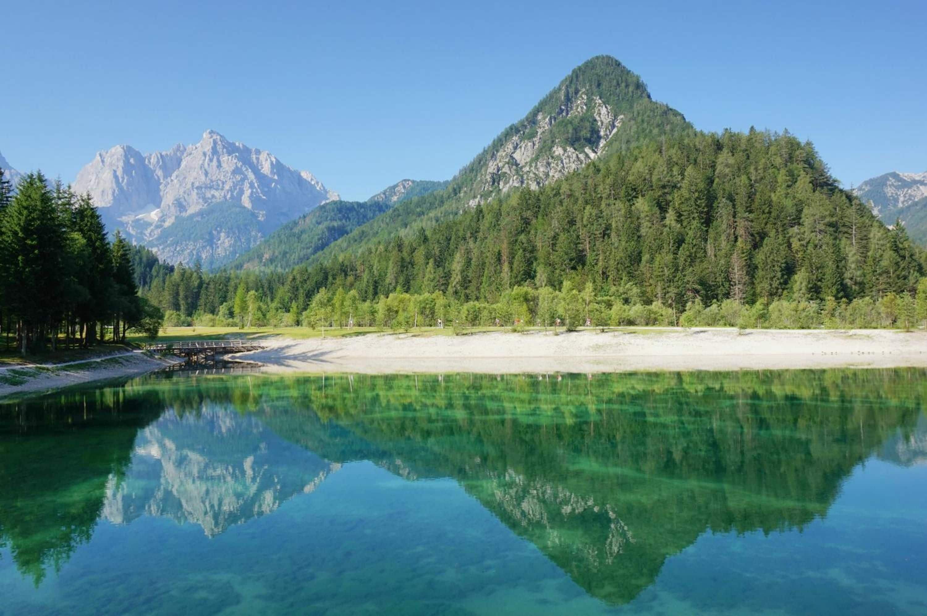 A tranquil lake with clear reflections, surrounded by dense forest and mountains.