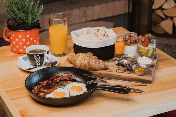 Une table de petit-déjeuner avec une poêle d’œufs, un croissant, un verre de jus d’orange, une tasse de café et une plante en pot.