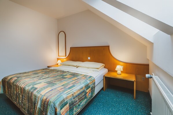 A bedroom with a bed, a nightstand, a lamp, a mirror, and a radiator. - Apartments Vitranc (Kranjska Gora)