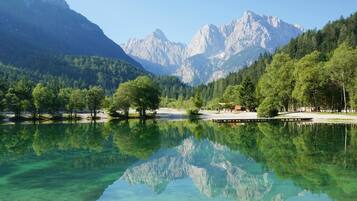A clear lake with reflections of trees and mountains, surrounded by a forested area and a walking path.