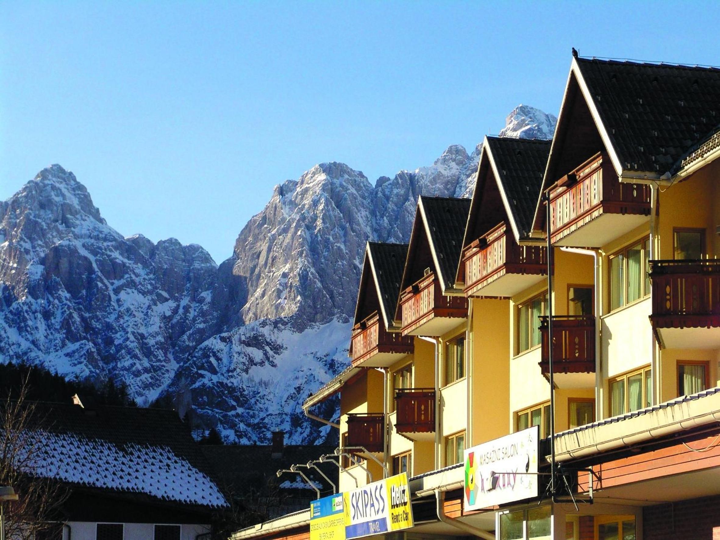 Un hotel con varios balcones, un letrero para alquiler de esquíes y un paisaje de montaña al fondo.