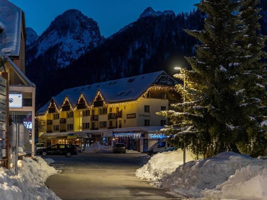 Un hotel con tejado cubierto de nieve, varios balcones y un paisaje montañoso de fondo.