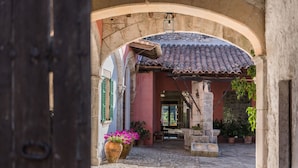 Un arco de entrada que da a un patio adoquinado con plantas en macetas y una estructura con tejado de baldosas.
