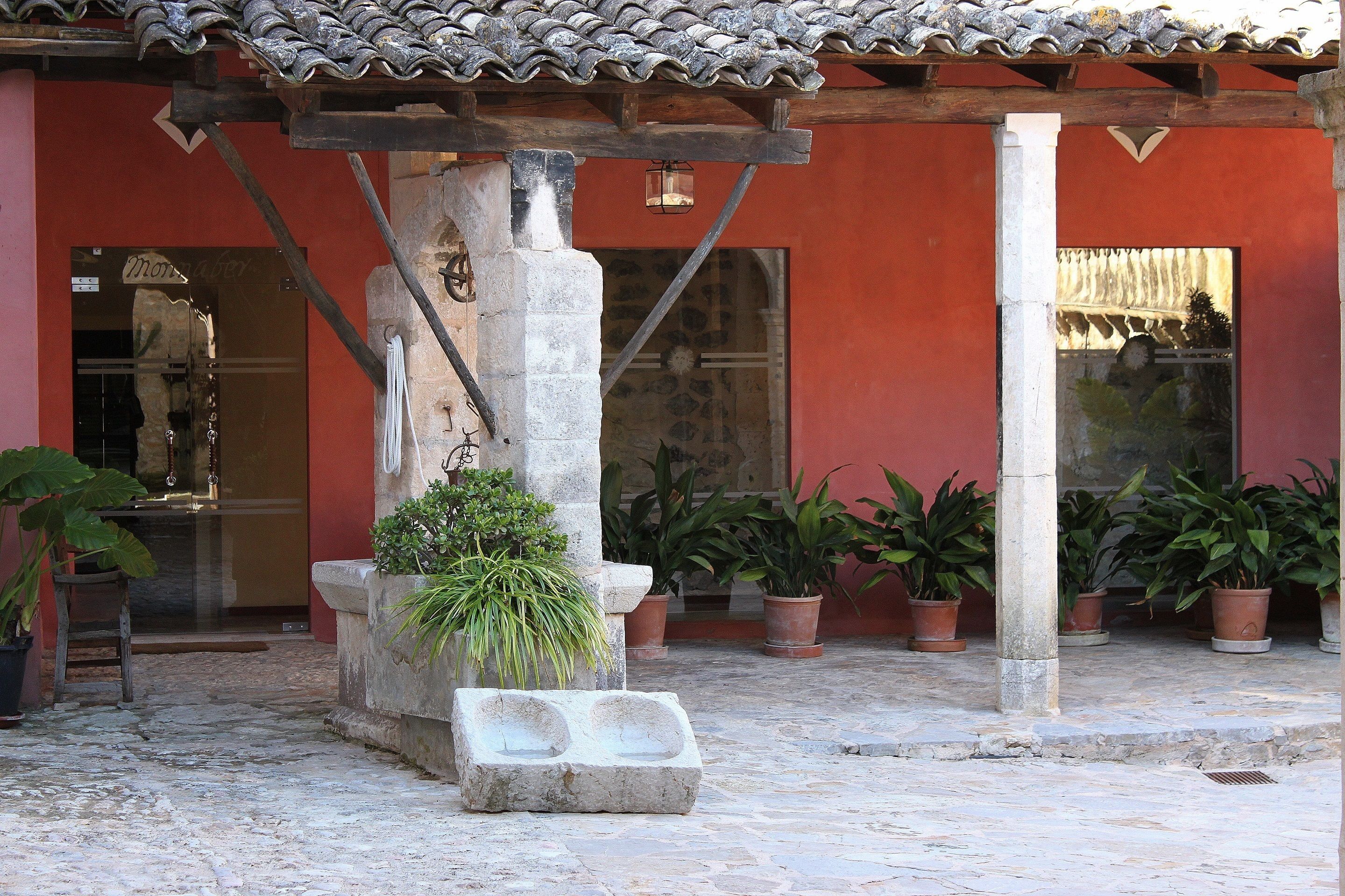 A courtyard with a tiled roof, potted plants, and a stone bench.