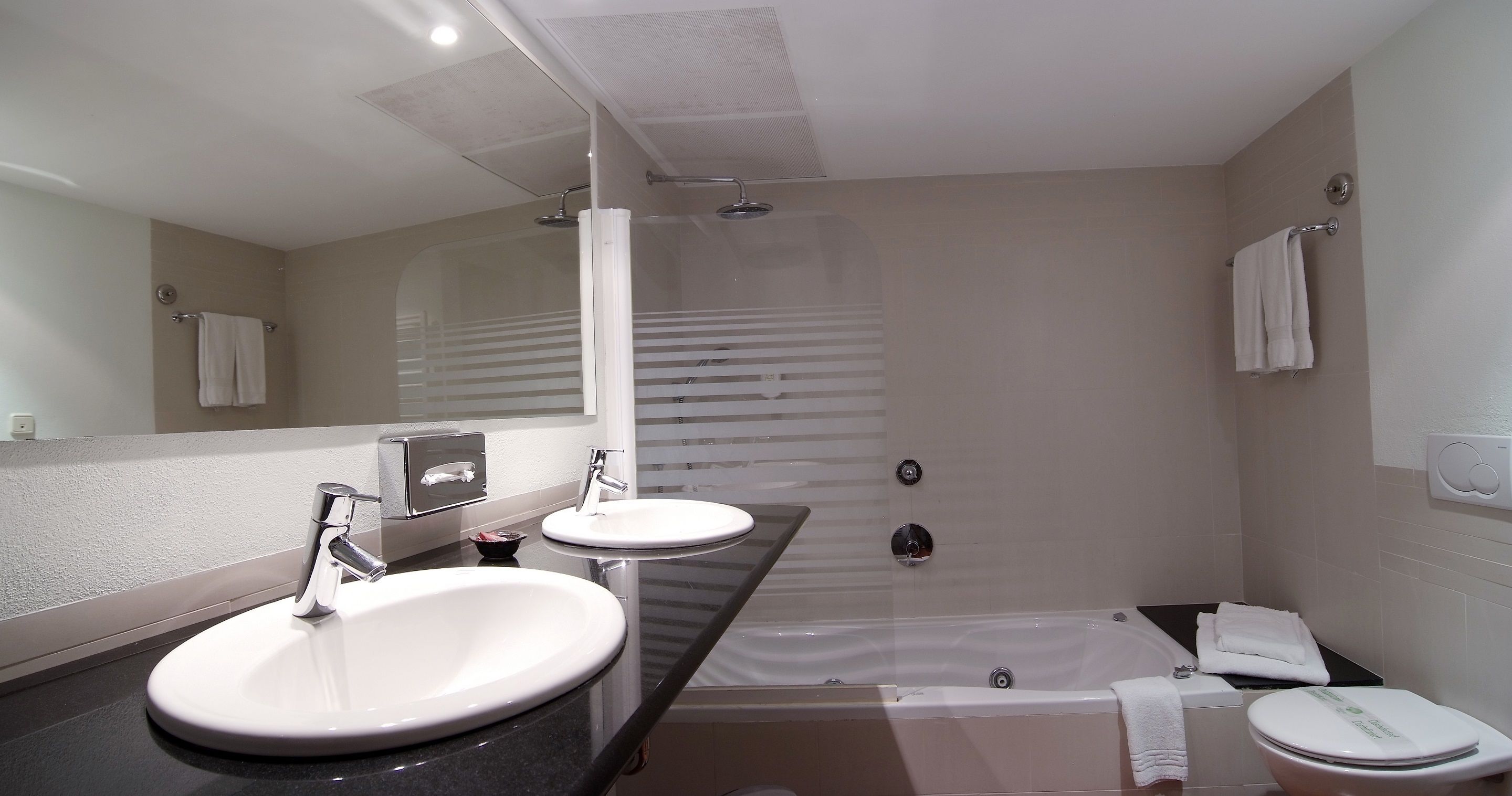 A modern bathroom with a double sink, a bathtub, and a toilet.