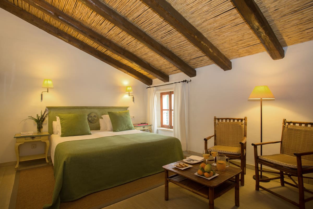 A bedroom with a bed, two chairs, a table with fruit and a drink, and two wall lamps.