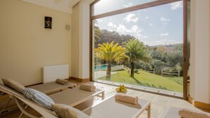 Un cuarto de spa con dos camillas de masaje, un ventanal con vistas a un jardín y árboles.