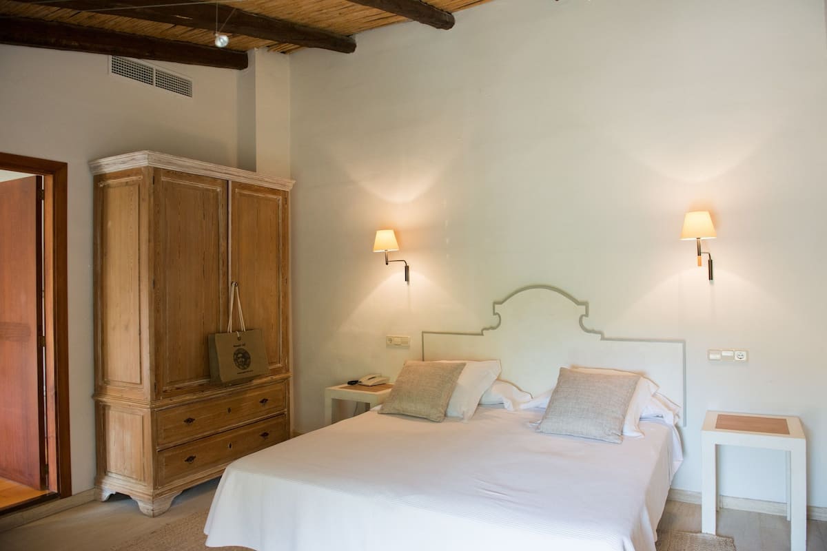 A bedroom with a large bed, wooden wardrobe, two bedside tables, and wall-mounted lamps.