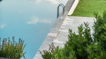 Una piscina rectangular con borde de piedra, rodeada de césped y árboles frondosos.