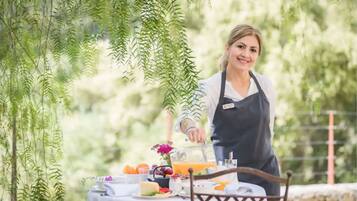 A person serving food at an outdoor table with a variety of dishes and a drink.
