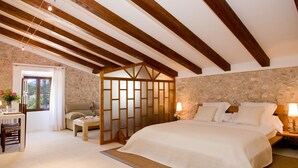 Un dormitorio con una cama grande, vigas de madera, pared de piedra y una ventana con cortinas.