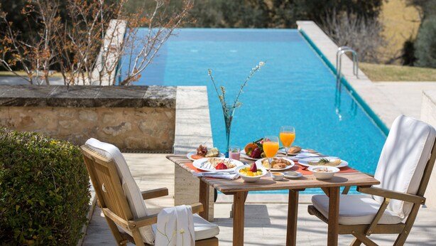Una mesa de comedor con platos, vasos y un jarrón de flores junto a una piscina.