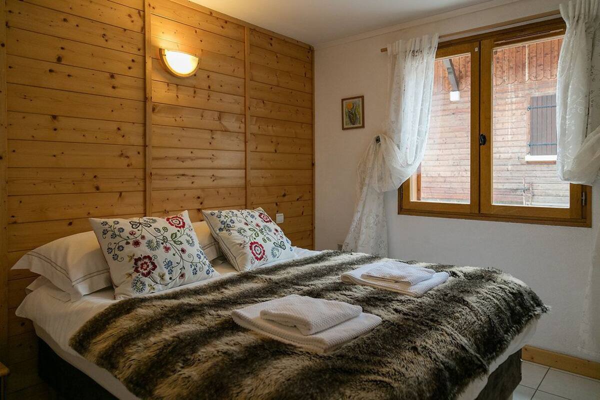 A wooden-paneled room with a bed, pillows, a blanket, and a window with curtains.