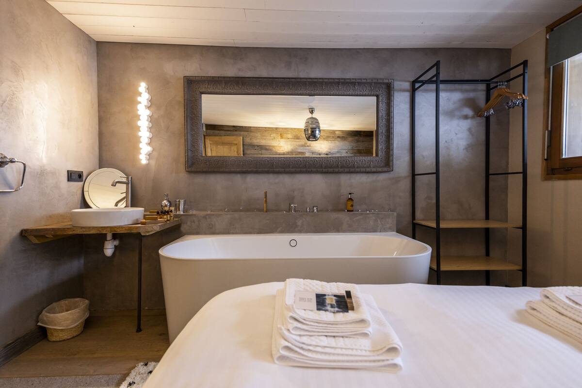 A modern bathroom with a large bathtub, a vanity with a mirror, and a wall-mounted light fixture.